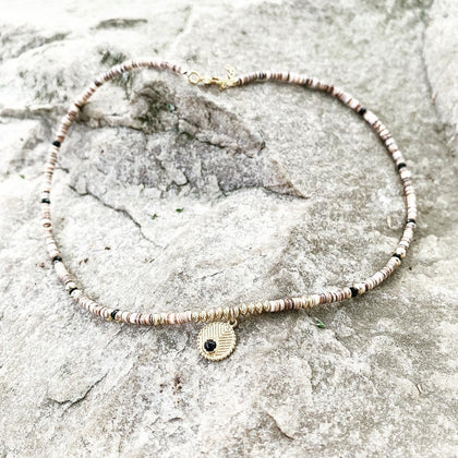 photo d'un collier en perle de coquillage et plaqué or avec pendentif plaqué or sur un support en pierre